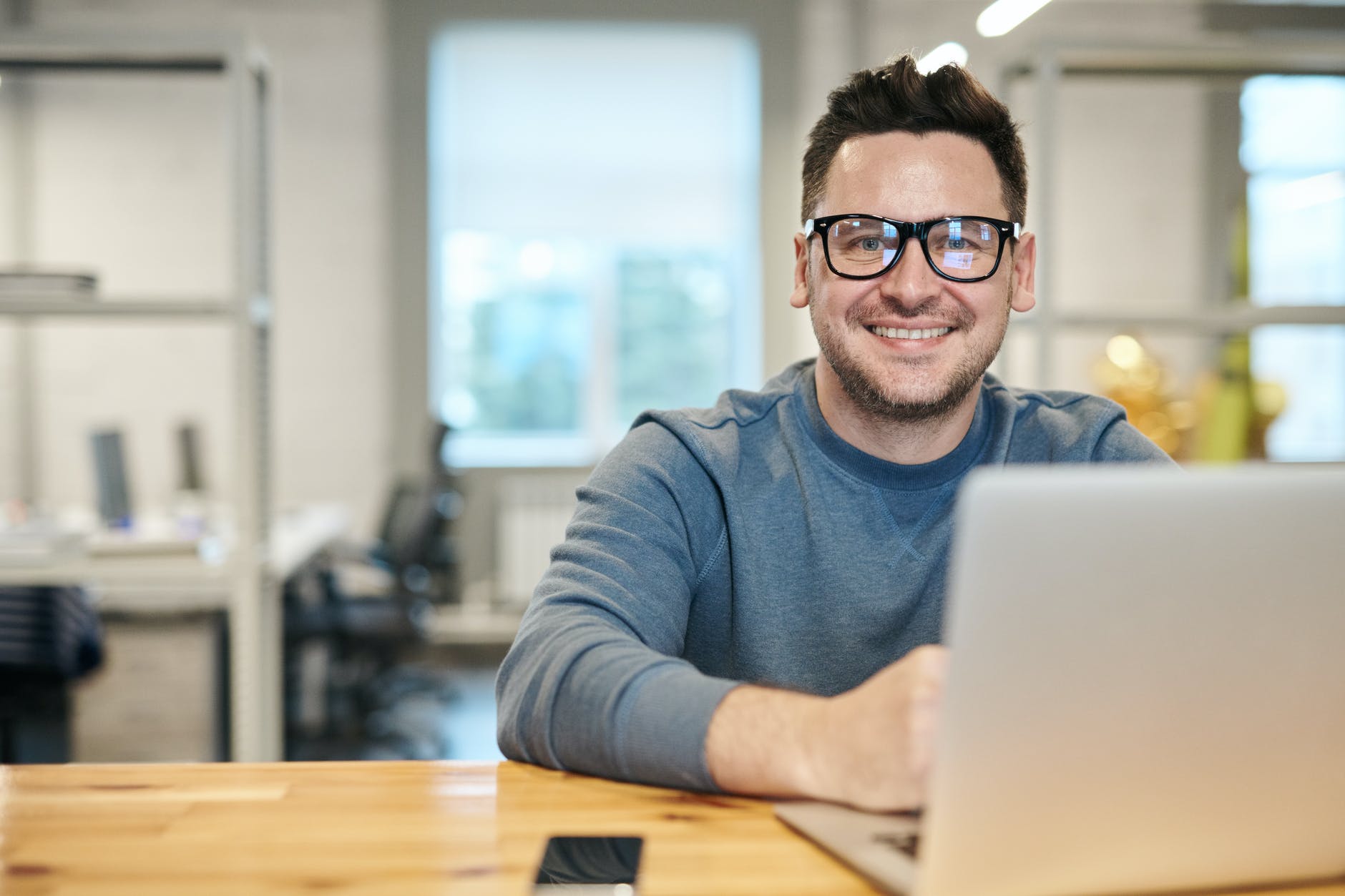 Smiling man with glasses sat down in front of laptop 