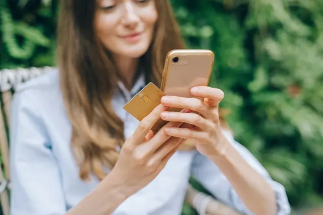 woman looking at her phone holding card