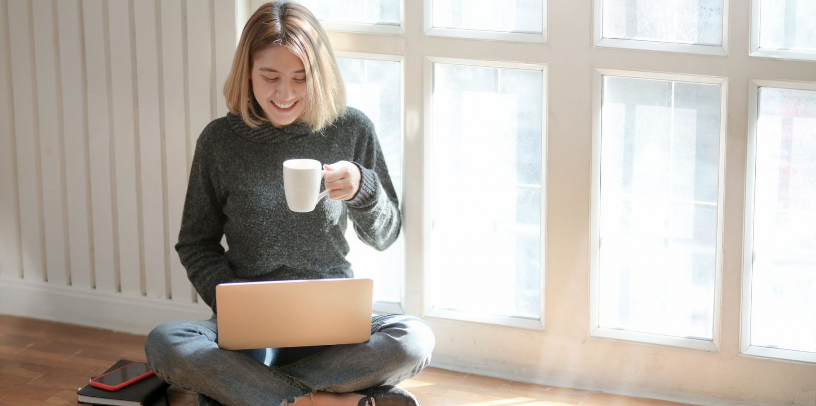 A woman drinking coffee while searching on her laptop